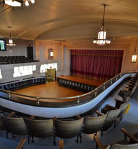 Elegant theater with tiered seating, central stage, red curtain, warm lighting, evoking nostalgia and anticipation for performances.