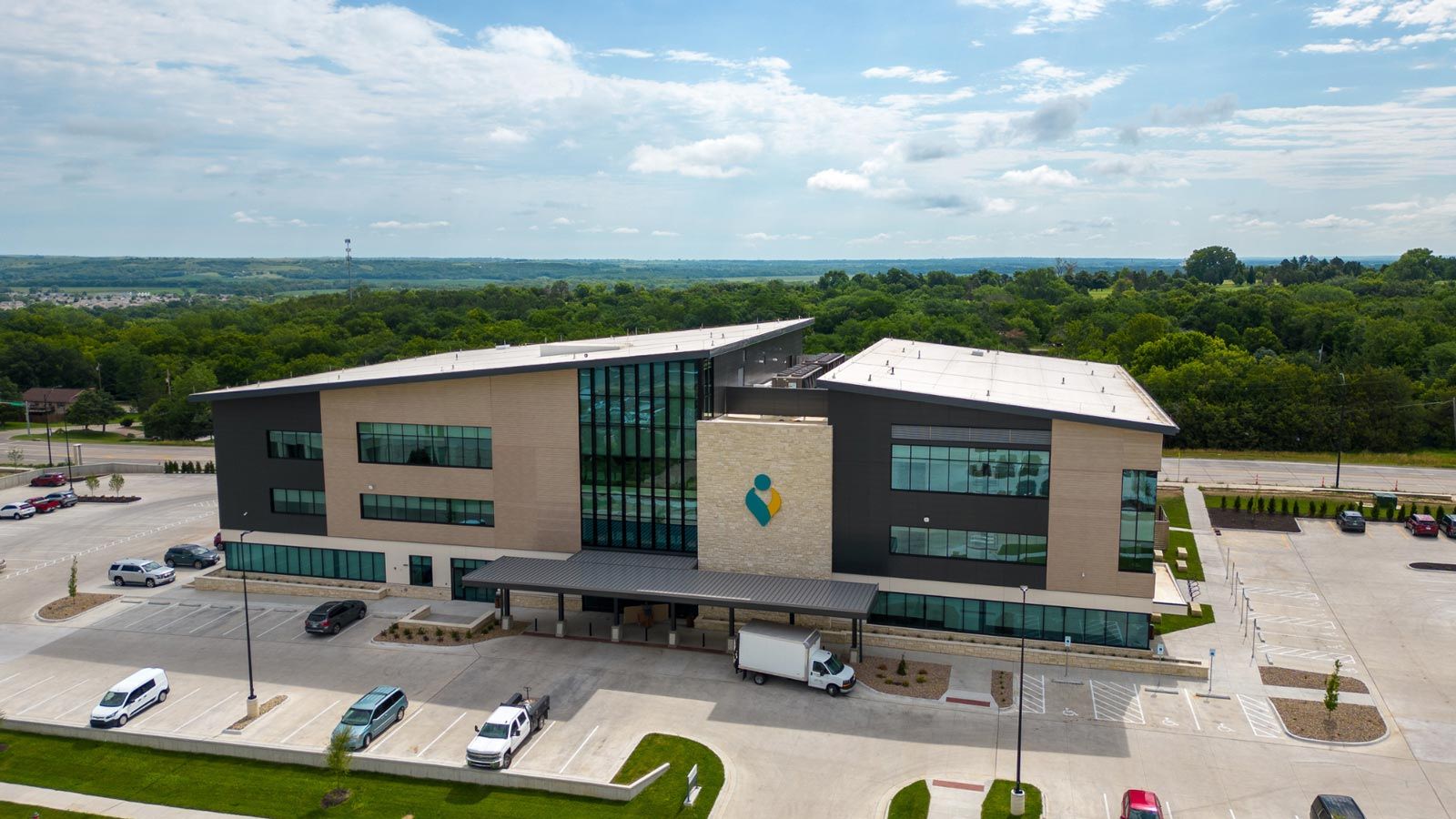 Modern building with glass, stone, and metal; surrounded by green hills and cars, conveying a serene, professional atmosphere.