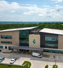 Modern building with glass, stone, and metal; surrounded by green hills and cars, conveying a serene, professional atmosphere.