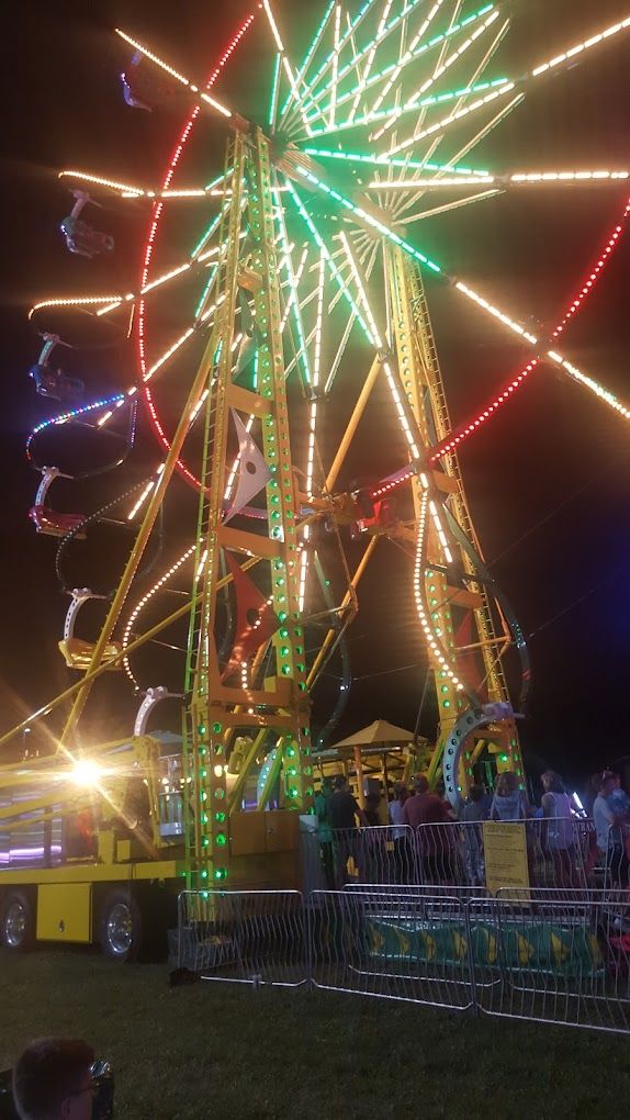 A colorful Ferris wheel lights up a lively night fair, evoking joy, nostalgia, and the spirit of community gatherings.