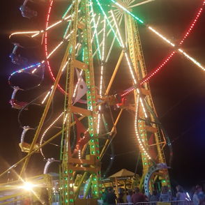 A colorful Ferris wheel lights up a lively night fair, evoking joy, nostalgia, and the spirit of community gatherings.