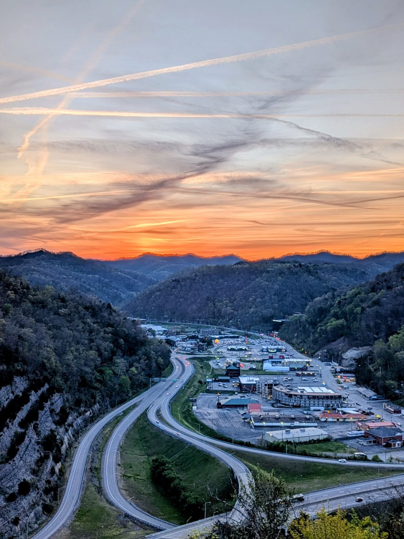 A serene sunset landscape with rolling hills, a winding road, and a mix of nature and urban life, evoking tranquility and reflection.