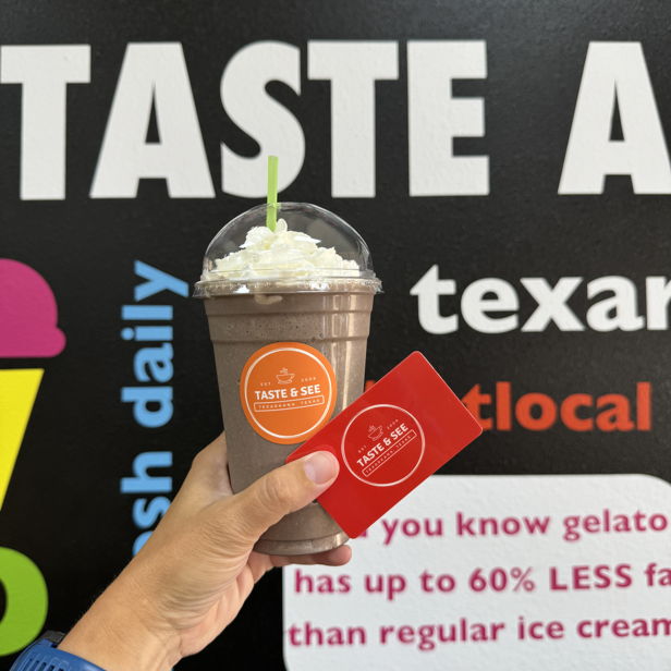 Hand holds a chocolate drink topped with whipped cream against a colorful, playful wall, evoking joy and indulgence.