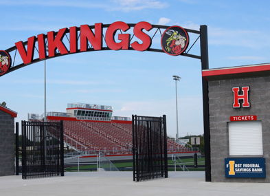 Entrance of a sports venue with a "VIKINGS" sign, ticket booths, and energetic colors, evoking community pride and excitement.