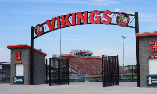 Entrance of a sports venue with a "VIKINGS" sign, ticket booths, and energetic colors, evoking community pride and excitement.