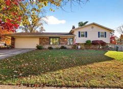 Charming suburban home amid vibrant autumn foliage, featuring brick siding, blue shutters, and a tranquil atmosphere.
