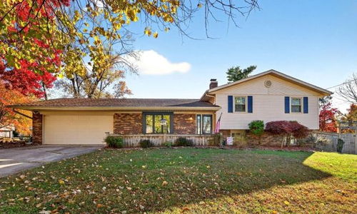 Charming suburban home amid vibrant autumn foliage, featuring brick siding, blue shutters, and a tranquil atmosphere.
