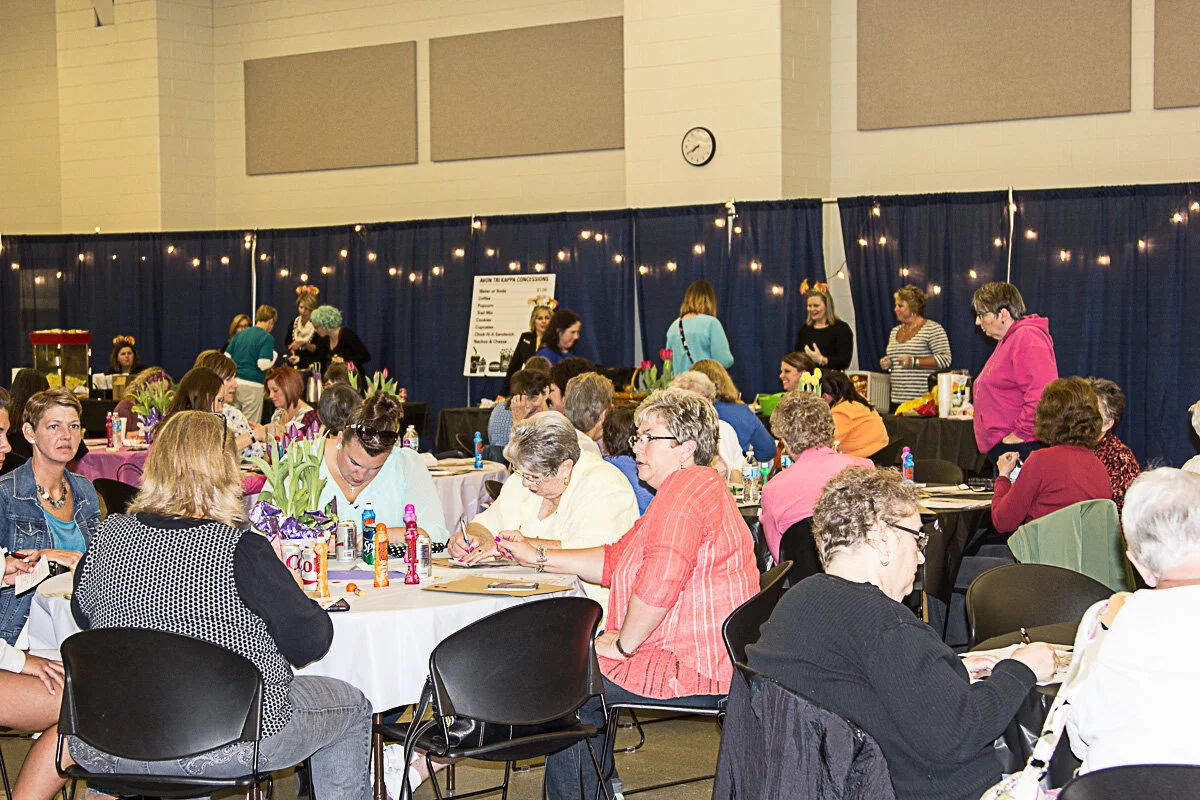 Lively gathering of mostly women at a community event, engaging in crafts with colorful decorations and a festive atmosphere.