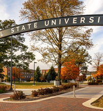 Welcoming entrance to Ball State University with an archway, pathways, trees, and vibrant campus, evoking openness and enthusiasm.