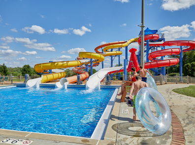 A vibrant water park scene with colorful slides, a clear pool, and people enjoying a sunny, adventurous day.