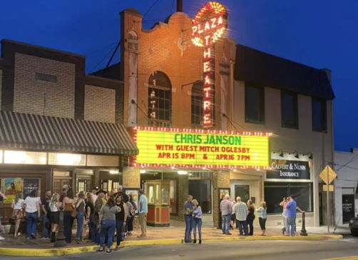 A lively theater scene at night with a bright marquee for Chris Janson, featuring a joyful crowd in a charming setting.