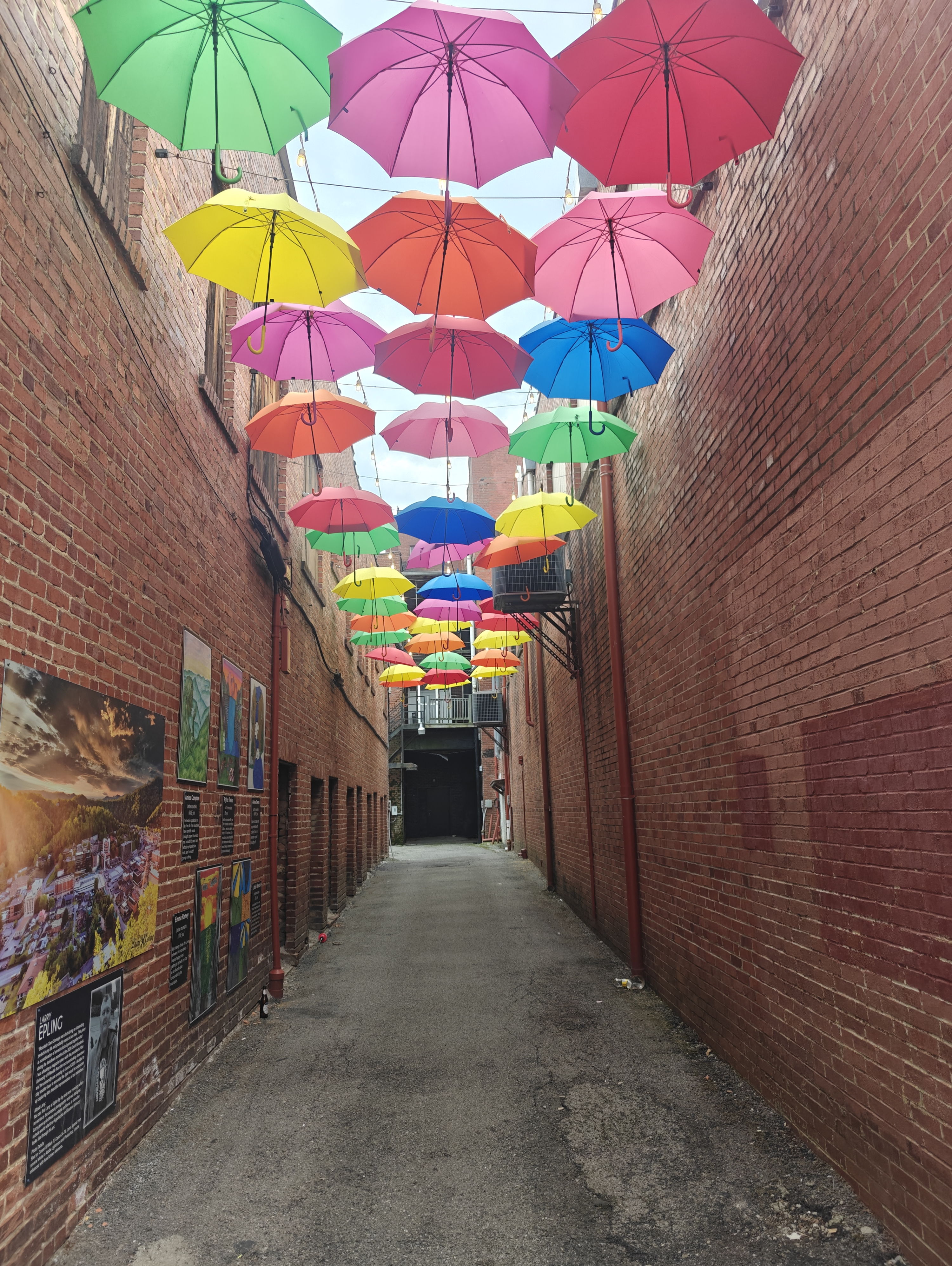 A vibrant alleyway with colorful umbrellas overhead and exposed brick walls creates a cheerful, whimsical atmosphere.