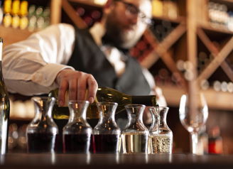 A bartender pours wine into decanters in a cozy bar, evoking sophistication, warmth, concentration, and celebration.