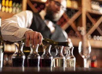 A bartender pours wine into decanters in a cozy bar, evoking sophistication, warmth, concentration, and celebration.