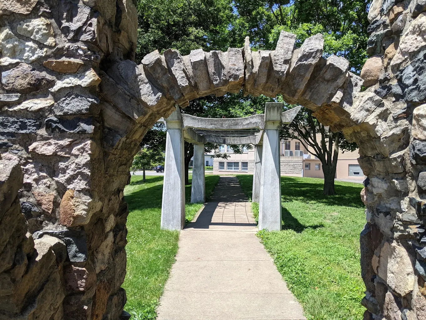 Stone archway leads to a serene park pathway, framed by vibrant greenery, evoking tranquility and a sense of adventure.