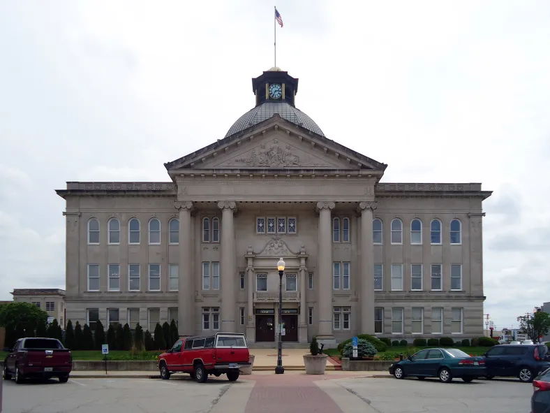 Classical government building with grand columns and dome, surrounded by cars, under a cloudy sky, evoking tradition and authority.