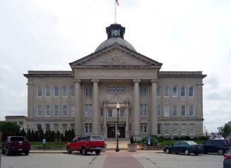Classical government building with grand columns and dome, surrounded by cars, under a cloudy sky, evoking tradition and authority.