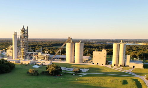 Industrial facility with silos and machinery set in green surroundings, blending productivity and nature’s tranquility.