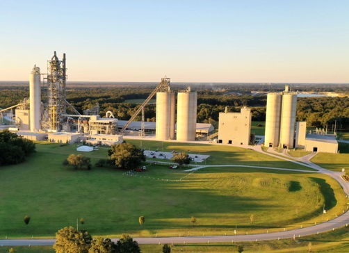Industrial facility with silos and machinery set in green surroundings, blending productivity and nature’s tranquility.