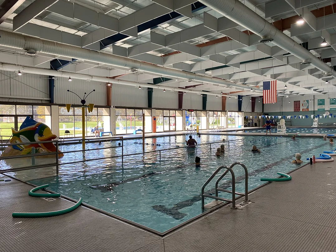 Indoor pool scene with people playing, colorful inflatables, bright lighting, evoking joy, fun, and community spirit.