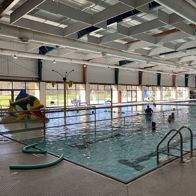 Indoor pool scene with people playing, colorful inflatables, bright lighting, evoking joy, fun, and community spirit.