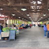 A lively indoor market scene with wooden beams, booths of goods, and people engaging, creating a cheerful community atmosphere.