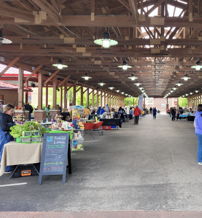 A lively indoor market scene with wooden beams, booths of goods, and people engaging, creating a cheerful community atmosphere.