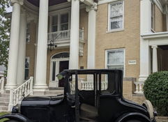 A classic two-story building with white pillars, large windows, and a vintage car, evoking nostalgia and elegance.