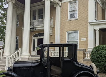 A classic two-story building with white pillars, large windows, and a vintage car, evoking nostalgia and elegance.