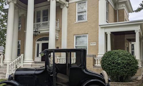 A classic two-story building with white pillars, large windows, and a vintage car, evoking nostalgia and elegance.