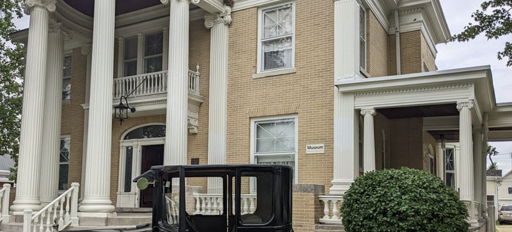 A classic two-story building with white pillars, large windows, and a vintage car, evoking nostalgia and elegance.