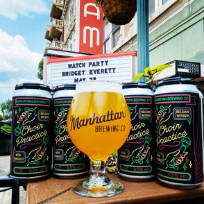 Colorful beer cans and a "Manhattan Brewing Co" glass set the scene for a festive watch party, evoking community and excitement.