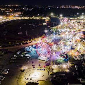 A vibrant carnival illuminated by lights features a Ferris wheel, rides, and food stalls, evoking joy and excitement.