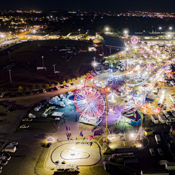 A vibrant carnival illuminated by lights features a Ferris wheel, rides, and food stalls, evoking joy and excitement.