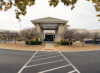 Modern building labeled "WILSON WESLEY" with stone accents, bare trees, and neat landscaping, conveying stability and warmth.