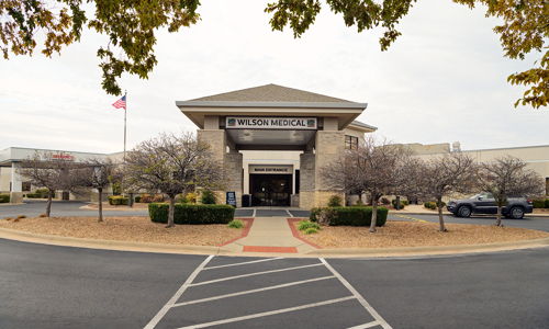 Modern building labeled "WILSON WESLEY" with stone accents, bare trees, and neat landscaping, conveying stability and warmth.