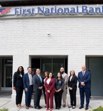A diverse, professional team stands confidently outside First National Bank, embodying teamwork, optimism, and community engagement.