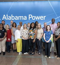 Diverse group smiling together in front of Alabama Power logo, reflecting teamwork and pride in a friendly atmosphere.