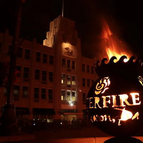 Stylized torch with dancing flames glows in a dark night, near a tall art deco building, evoking warmth and celebration.