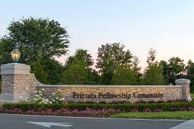 Entrance gate to Friends Fellowship Community, featuring stone, greenery, flowers, and a warm twilight atmosphere.