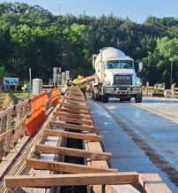 Construction site with a cement truck, wooden structures, and safety barriers amidst lush trees, symbolizing industry and progress.