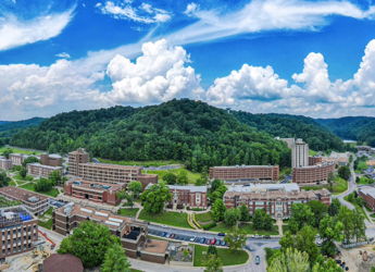 Vibrant campus view with green hills, blue sky, and modern buildings, evoking tranquility and harmony with nature.