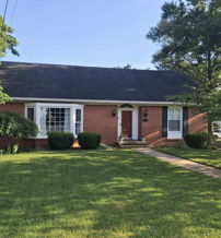 Charming single-story brick house with a lush lawn, trees, and blue sky, evoking warmth and a sense of home.