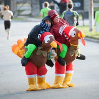 Two individuals in colorful turkey costumes embrace playfully at a festive running event, radiating joy and camaraderie.