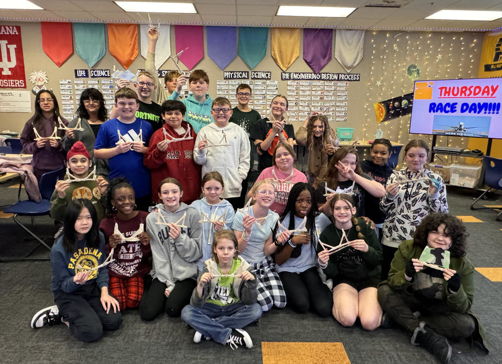 Students gather in a colorful classroom, joyfully posing with smiles, suggesting celebration and camaraderie.