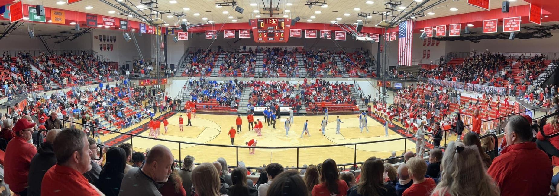 A lively sports arena brimming with enthusiastic fans in red, showcasing excitement and community pride before a basketball game.