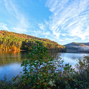 A serene landscape features a lake, vibrant autumn foliage, and rolling hills, evoking peace and appreciation for nature.
