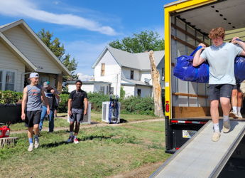 A group of young people collaboratively unload a truck on a sunny day, showcasing teamwork and a sense of new beginnings.
