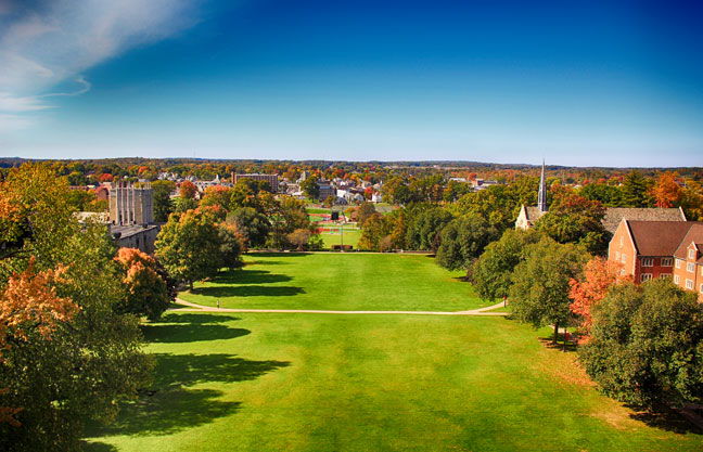 Vibrant campus scene with autumn foliage, green lawns, historic buildings, and a clear blue sky, evoking calmness and nostalgia.