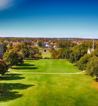 Vibrant campus scene with autumn foliage, green lawns, historic buildings, and a clear blue sky, evoking calmness and nostalgia.